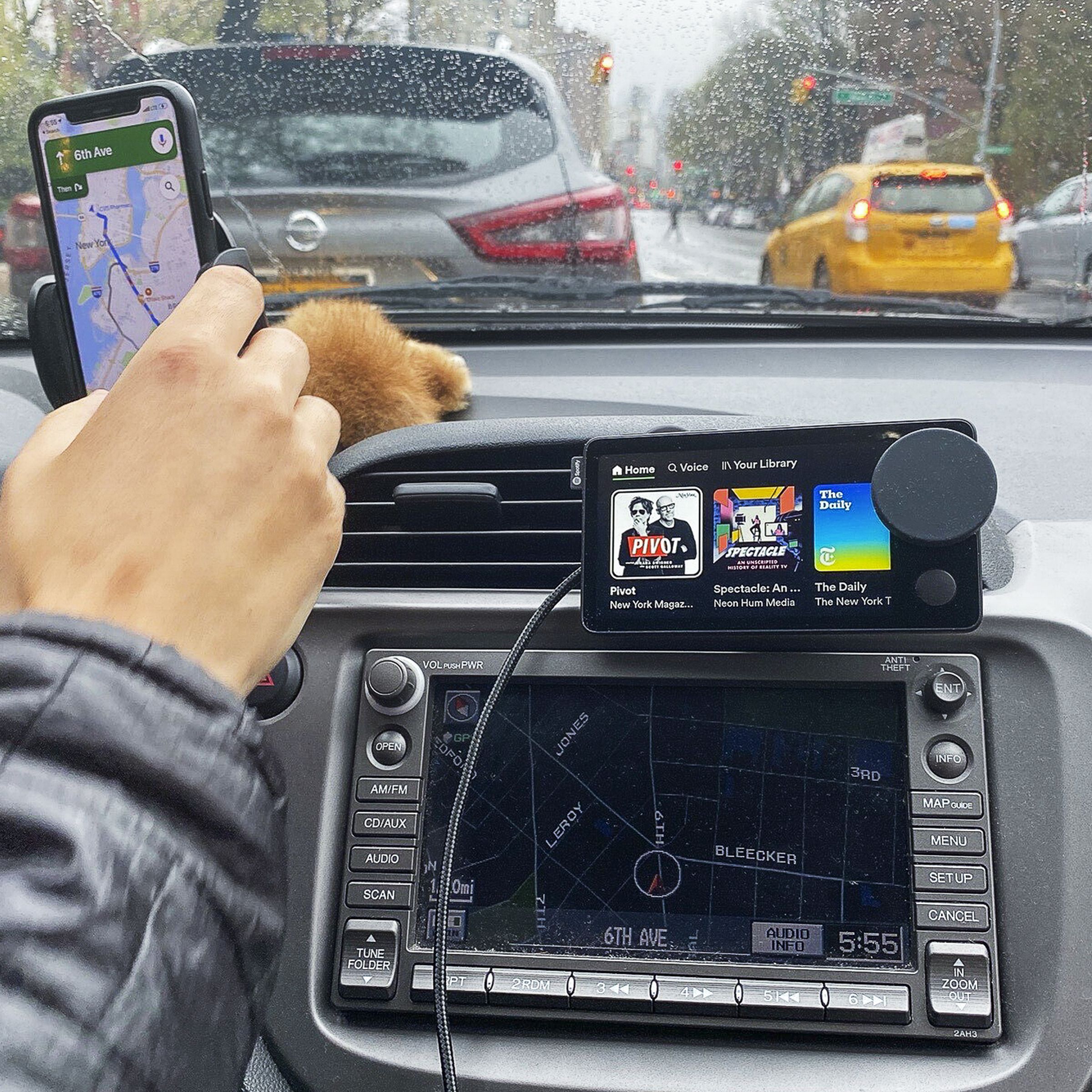 A driver in a car using a Spotify Car Thing and smartphone mounted to the dashboard.