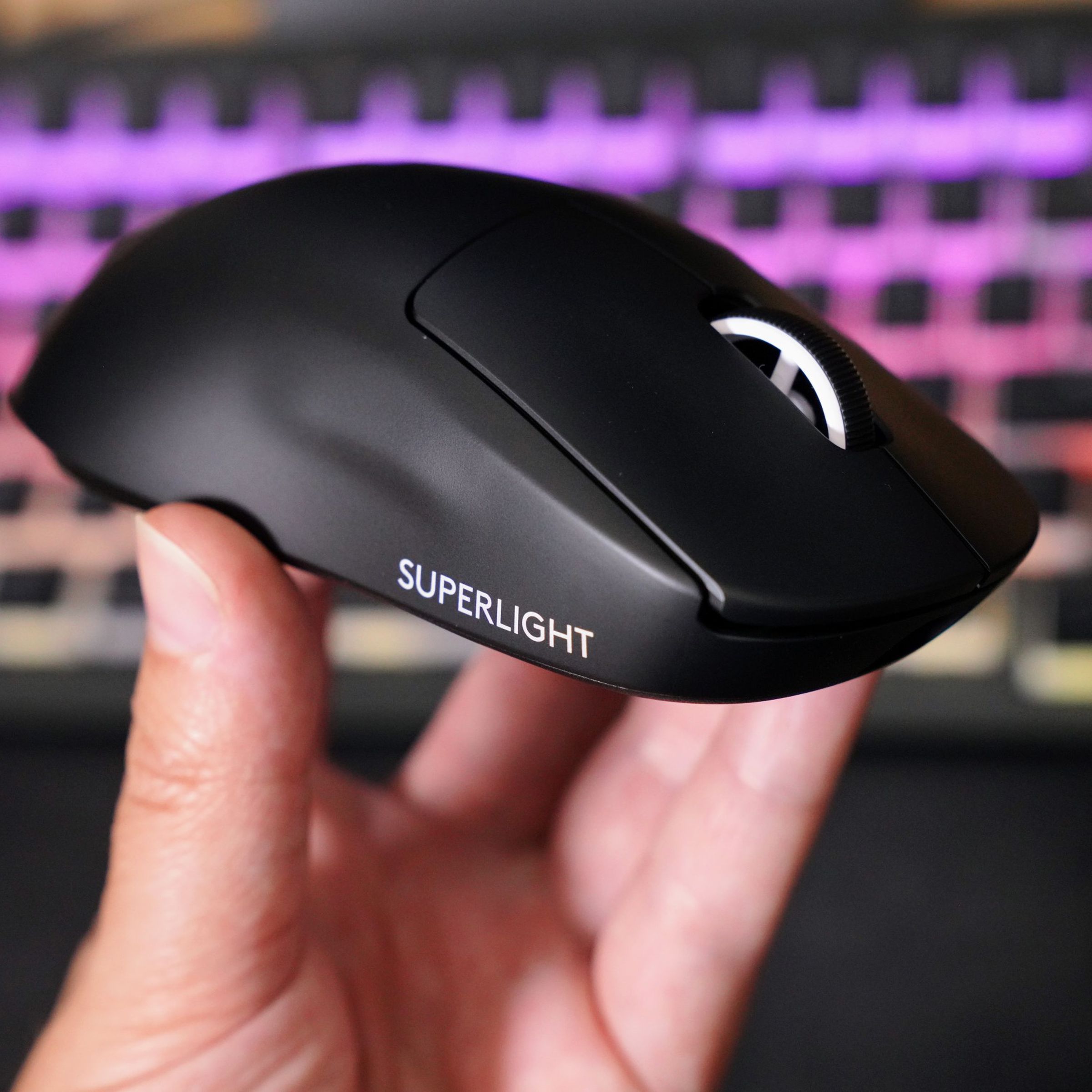A hand holds up a jet black sculpted plastic mouse with a white scroll wheel and white words “Superlight” printed on the side.