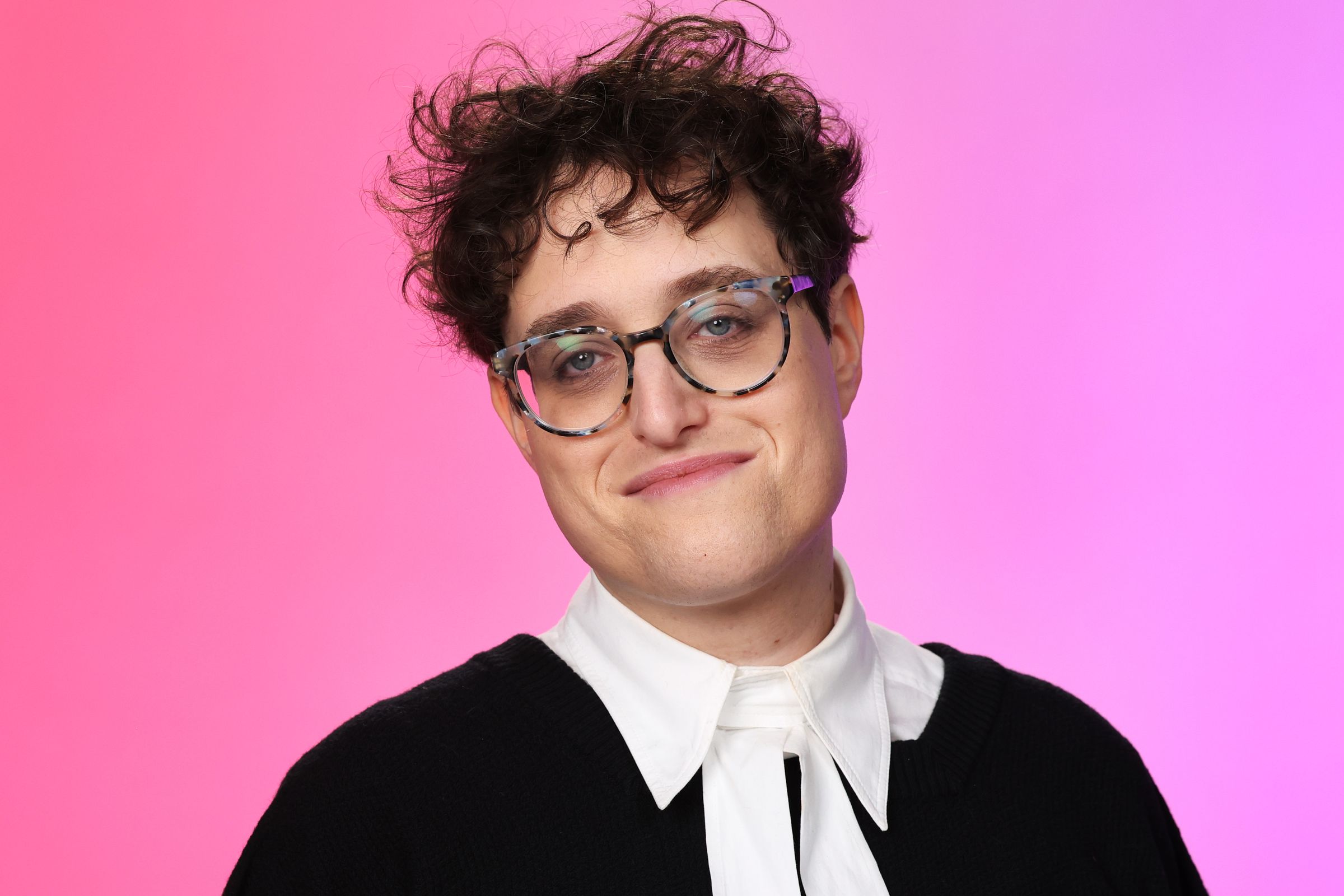 A close-up portrait shot of a nonbinary person wearing glasses, and a frock that resembles that of a court judge.