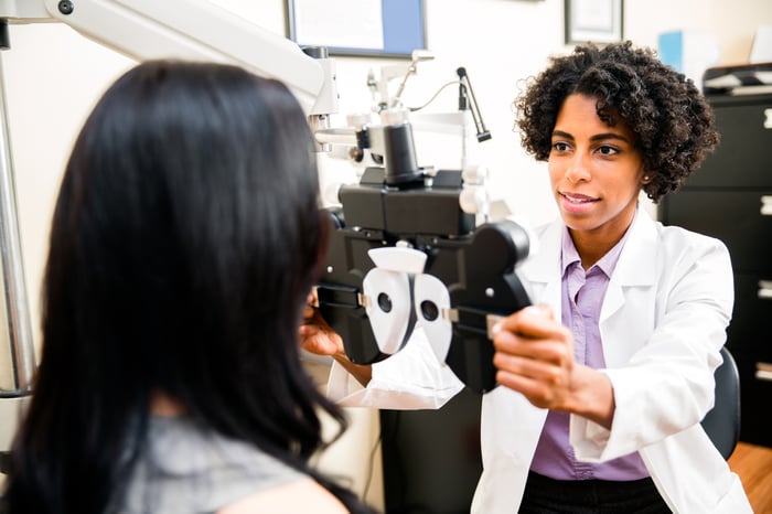 Eye doctor brings a machine up to a patient's face in a medical office.