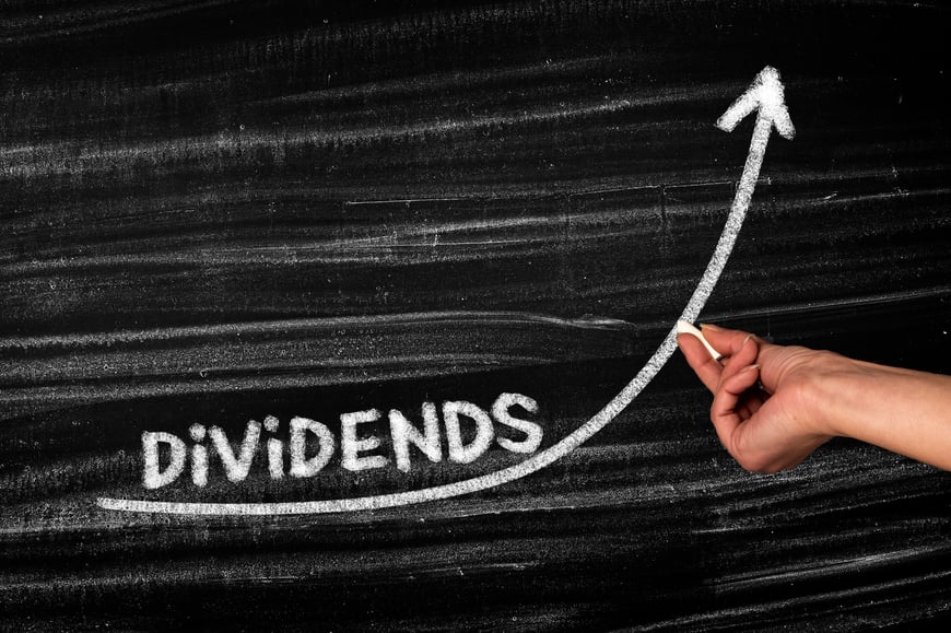 The word dividends on a chalkboard with a person drawing an upward arrow.