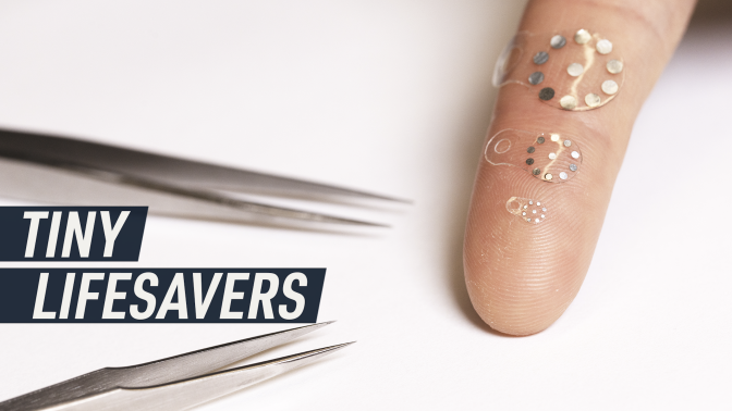 A white background photograph shows a couple of medical tweezers next to three of the tiny stickers placed on an index finger for scale.