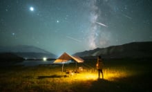 a person standing at a campsite as meteors streak overhead