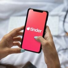 A person holding a phone showing the Tinder logo.