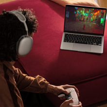 an over-the-shoulder view of a person playing video games on an m3 apple macbook while wearing a pair of airpods max