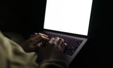 A pair of hands typing on a laptop in the dark.
