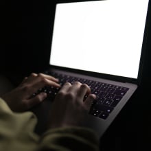 A pair of hands typing on a laptop in the dark.