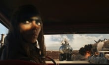 Furiosa backs a car away from a cliff and other burning cars.