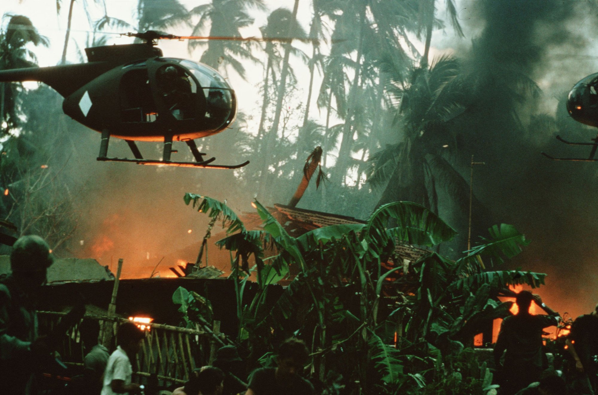 A helicopter hovers over fires in a jungle