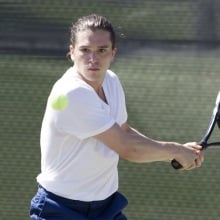 A tennis player in a white shirt hits a ball.