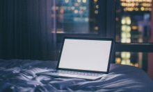 laptop with white screen on bed, city night scene in window