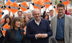 The three politicians smiling in front of a crowd of people holding Lib Dem posters