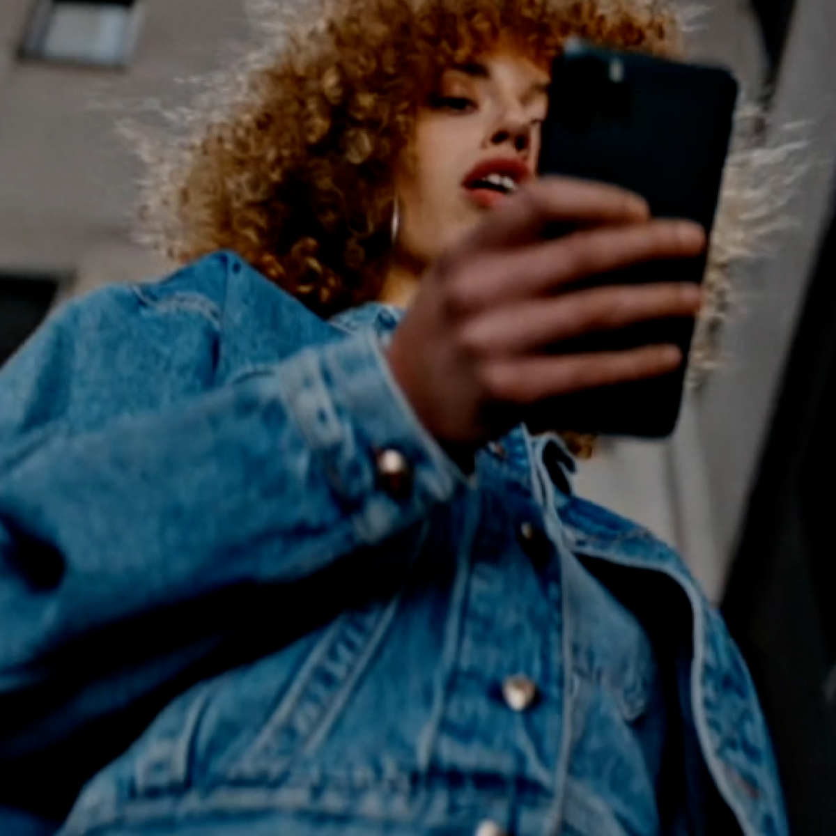 Woman with curly hair looking down at her mobile phone