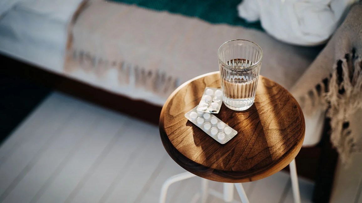 sleeping pills and water glass on stool next to bed