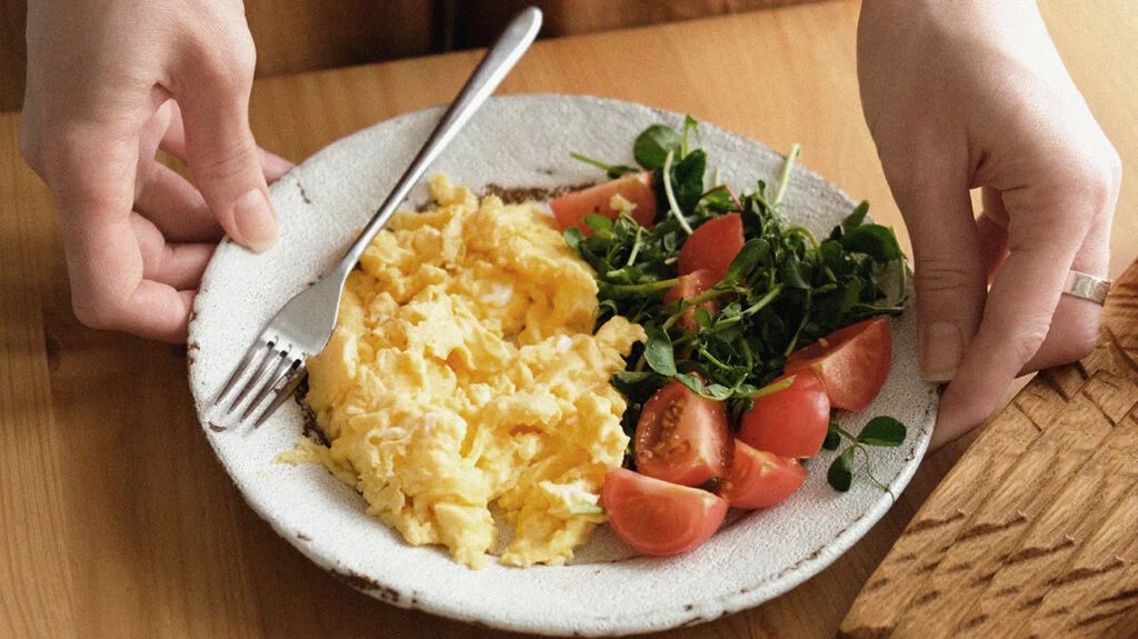a plate of scrambled eggs, tomatoes, and cooked spinach, which are foods suitable for a lazy keto diet