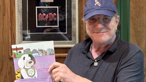Brian Johnson holding up the book called Bobby's Big Day Out 