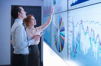 [Featured image] Two data scientists examine graphs and charts on a large white board