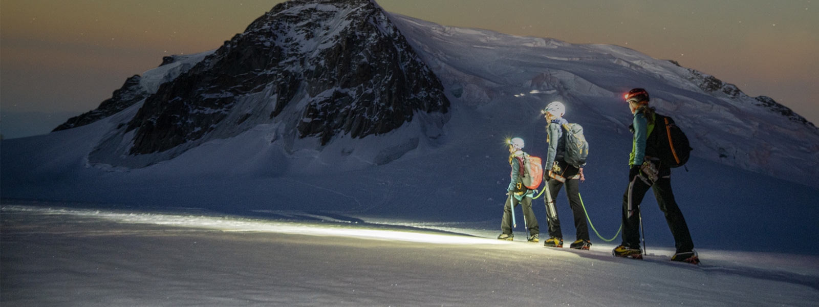 Tre escursionisti che percorrono una montagna innevata sotto un cielo stellato