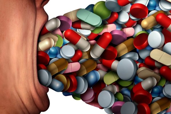 Too many pills health risk symbol and pharmaceutical overdose or overprescribed prescription drugs conceptas a person with a huge open mouth ingesting excessive amounts of medication as a metaphor for medicine with 3D illustration elements.