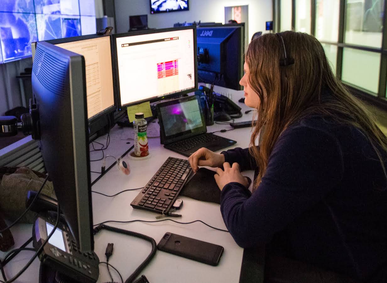 En ung kvinde sidder ved et skrivebord og arbejder foran tre skærme.