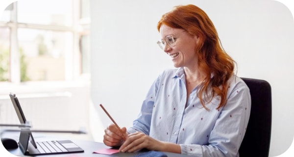 En kvinna ler under ett Meet-samtal och gör anteckningar 