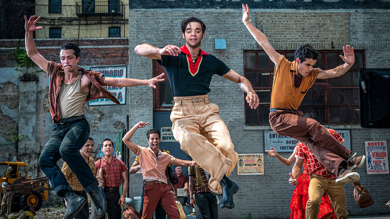 Actor David Alvarez jumping in the air while dancing alongside two others from the 20th Century Studios movie "West Side Story".