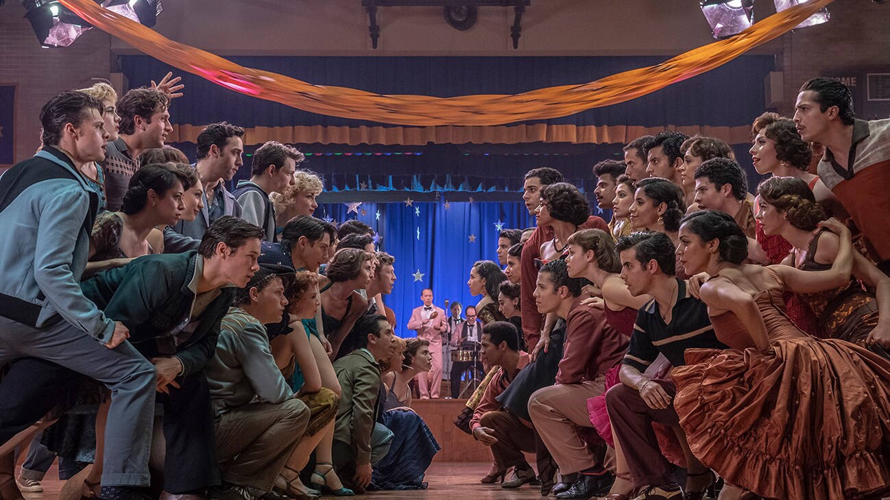 Two groups of people staring at each other while standing and kneeling on a dance floor from the 20th Century Studios movie "West Side Story".
