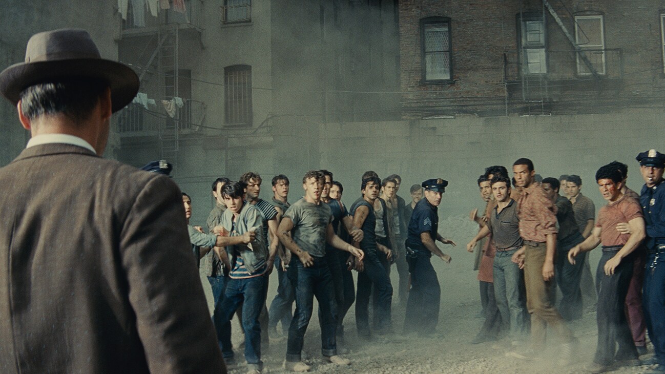 Actors Brian d'Arcy James and Corey Stoll among a group of young men and police outside an apartment complex from the 20th Century Studios movie "West Side Story".