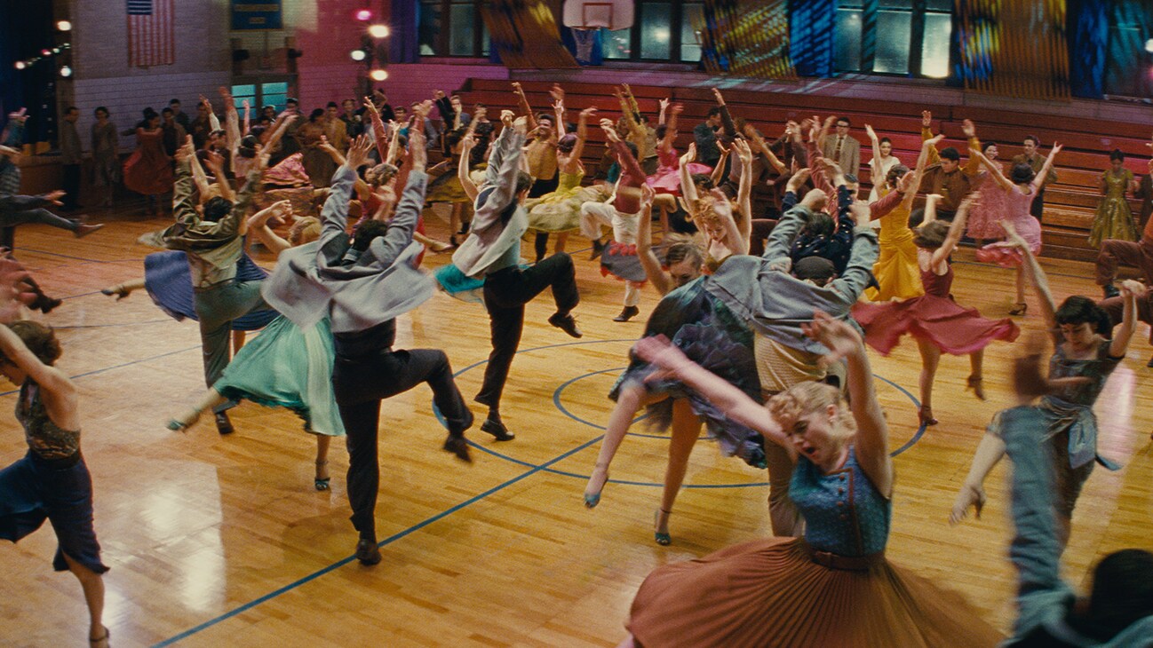 A group of people dancing in an indoor basketball court from the 20th Century Studios movie "West Side Story".