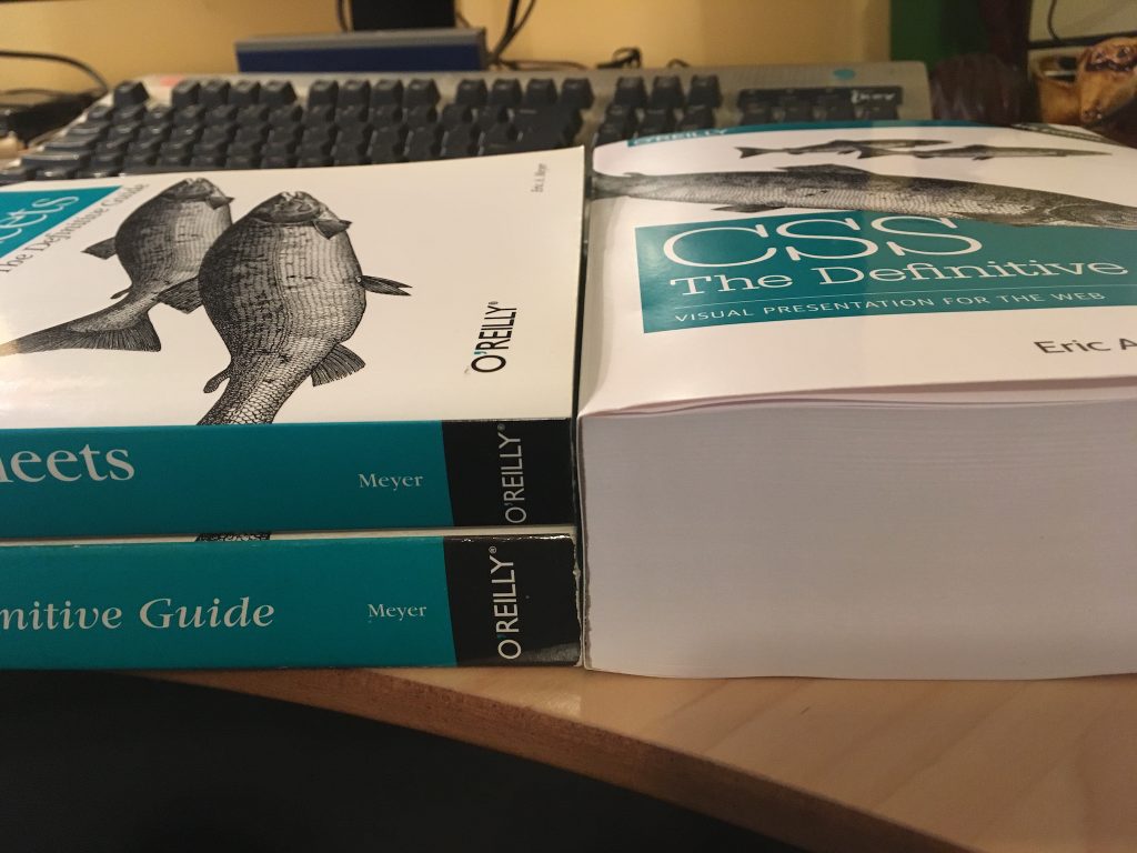 The fourth edition of “CSS: The Definitive Guide” sits on a desk to the right. To the left are the second and third editions of the same book, one atop the other. The two stacked books are, together, almost exactly the same height as the single book on the right.