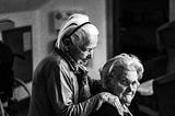 A woman hugs an older woman from behind. Black and white photo.