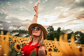 Woman in red dress standing in a firld of sunflowers pointing up.