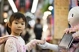 Young girl interacting with a humanoid robot adorned with pink flowers in a busy market setting.