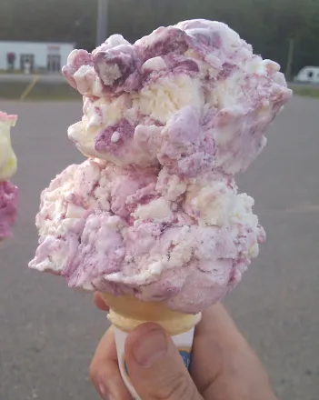 Two scoops of pink and cream ice cream piled onto a wafer cone.