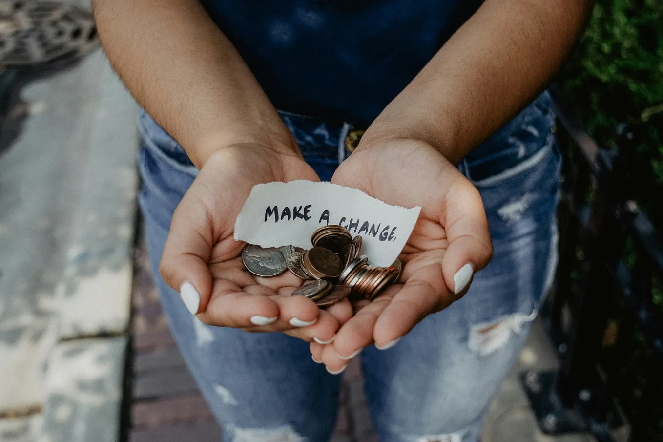 coins are held in open palms with a sign that reads, “make a change.”