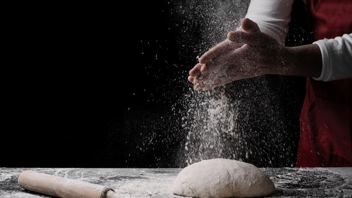 baker preparing bread dough on black table in front of yellow background