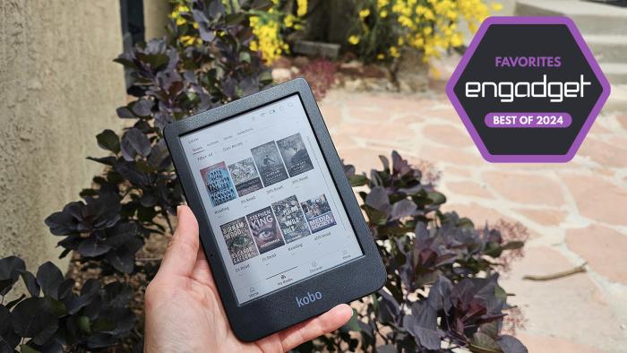 A person holds an ereader in front of some bushes. 