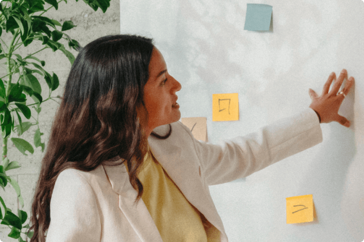Smiling woman in business attire discussing sticky notes on a board