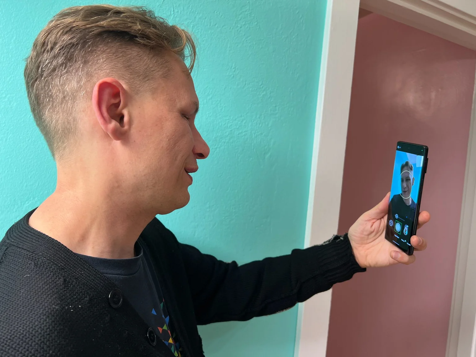 A photo of a man taken from a profile view. He is holding up his phone to take a selfie using Guided Frame.