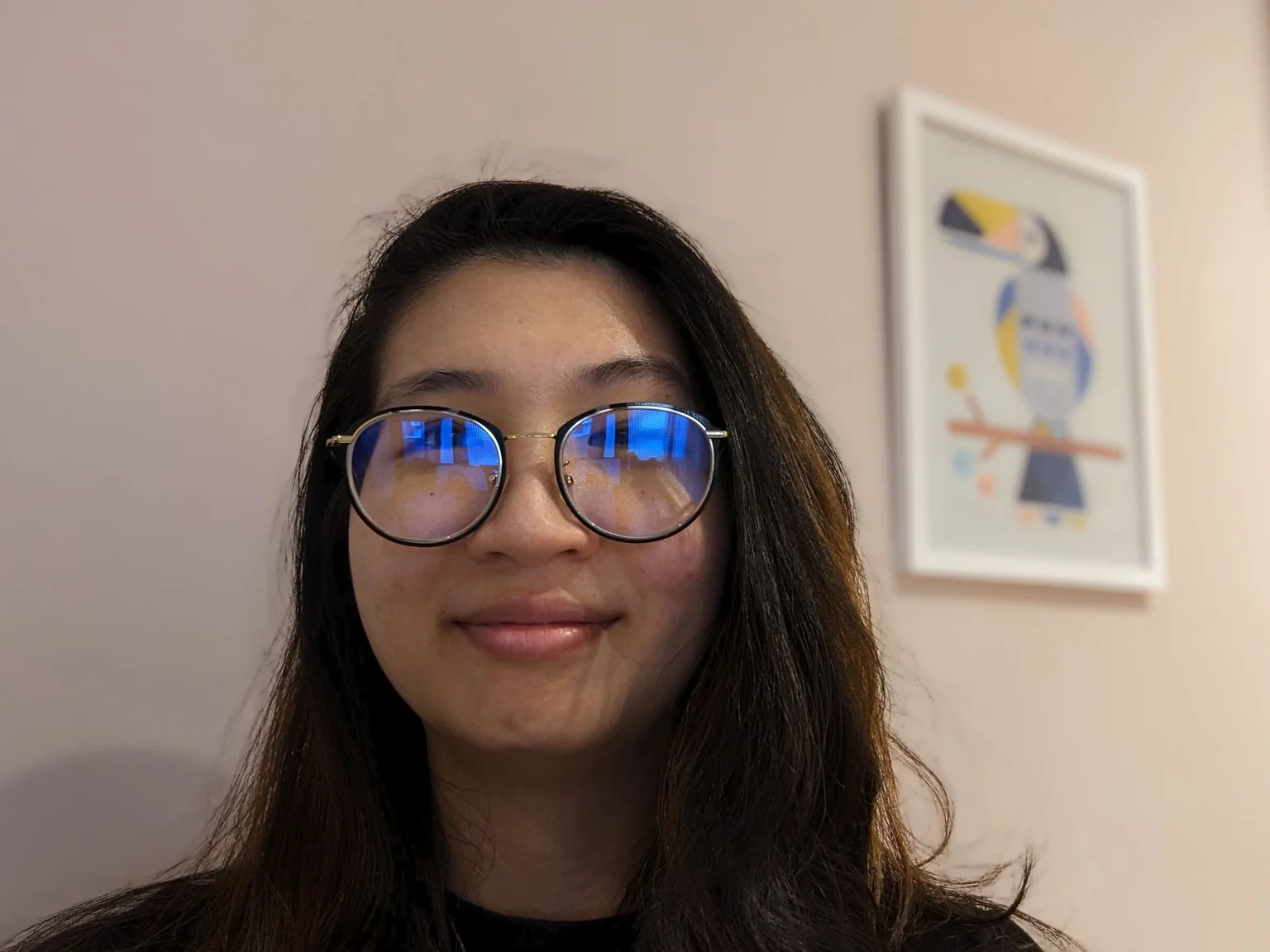 A woman looking into the camera and smiling; in her glasses you can see the slight reflection of the Guided Frame app on her phone, which she is using to take this selfie.