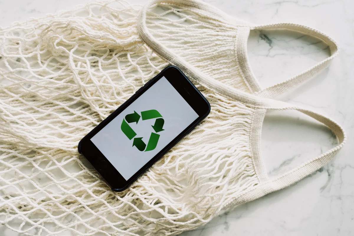 A phone with the recycling logo on it agains the backdrop of a reusable bag.
