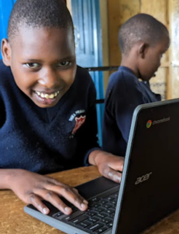 A young boy sits and is smiling widely as he places his hands on his brand new Chromebook laptop