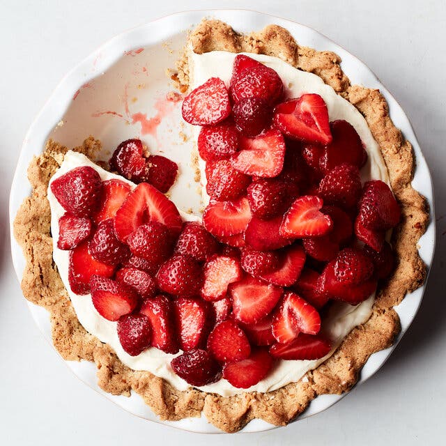 An overhead image a creamy pie topped with tons of halved strawberries. A serving sits just to the left.