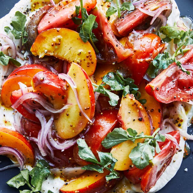 An overhead image of tomatoes and peaches on a bed of goat cheese.