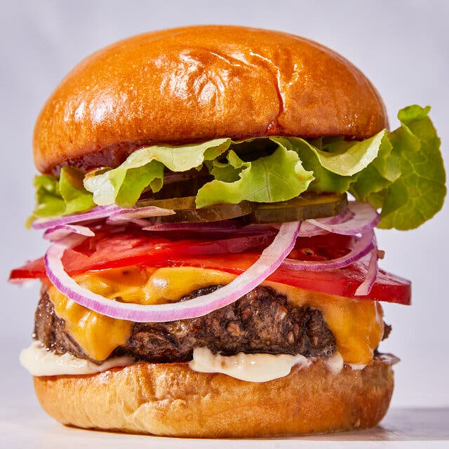 A burger stacked with cheese, tomatoes, onions, pickles and lettuce is photographed from the side.